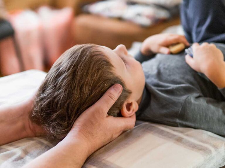 A person gently stretching their lower back on a living room floor with a soft mat and sunlight streaming through a window.